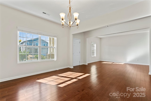 empty room with dark wood-type flooring, a wealth of natural light, and a notable chandelier