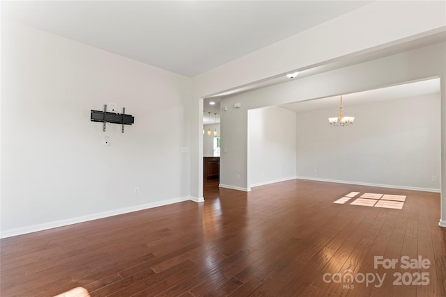 spare room with dark hardwood / wood-style floors and an inviting chandelier