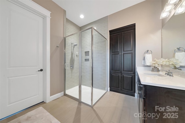 full bath with a shower stall, vanity, baseboards, and wood finished floors