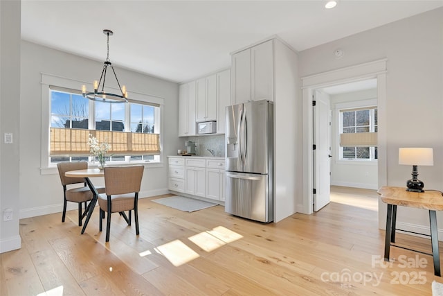 kitchen featuring white microwave, light wood-style flooring, tasteful backsplash, and stainless steel fridge with ice dispenser