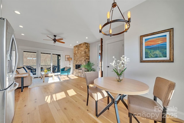 dining room with ceiling fan with notable chandelier, light wood-style flooring, recessed lighting, and a fireplace