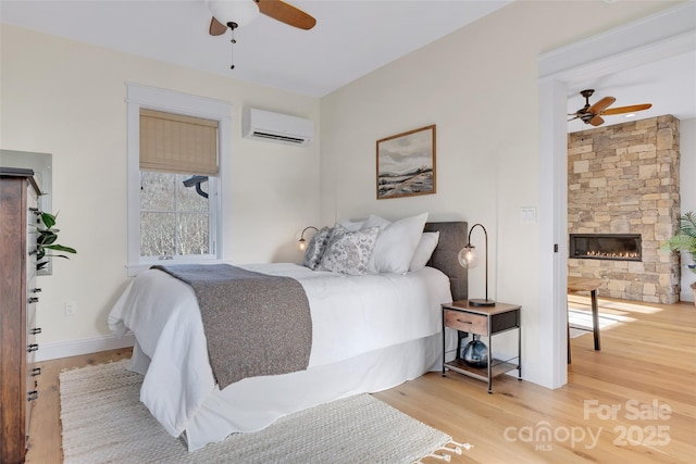 bedroom with a ceiling fan, wood finished floors, a wall unit AC, a fireplace, and baseboards