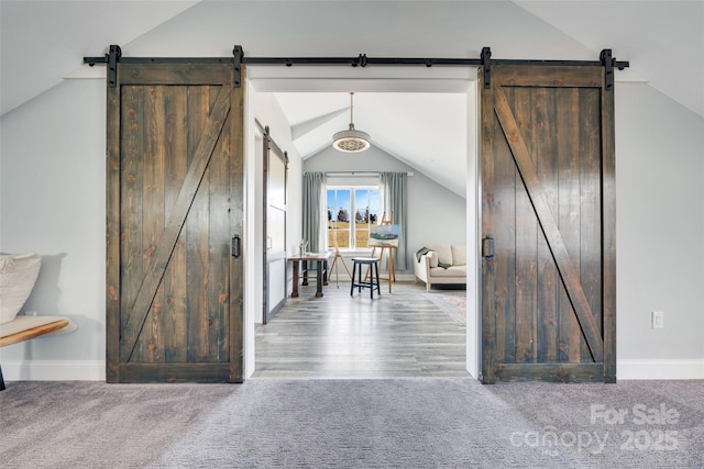 interior space with carpet flooring, baseboards, a barn door, and vaulted ceiling