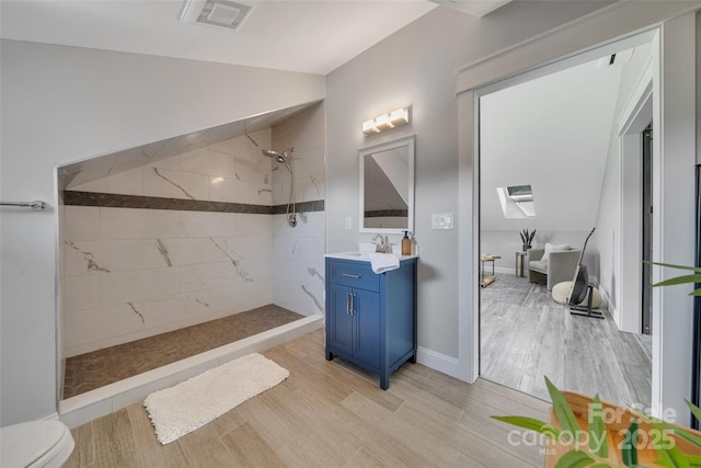 full bathroom with visible vents, toilet, a tile shower, wood finished floors, and vanity