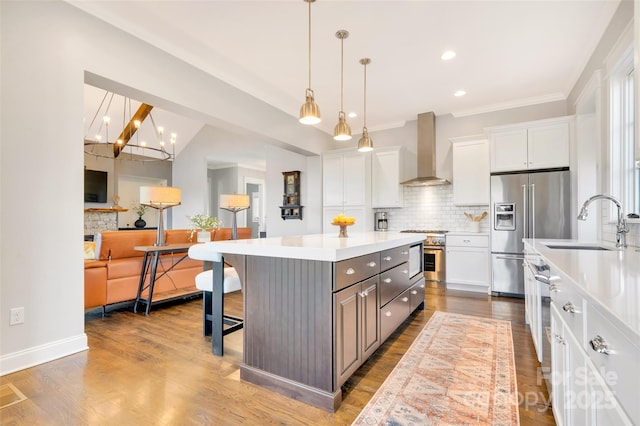 kitchen featuring a sink, white cabinetry, wall chimney exhaust hood, stainless steel fridge, and a kitchen bar