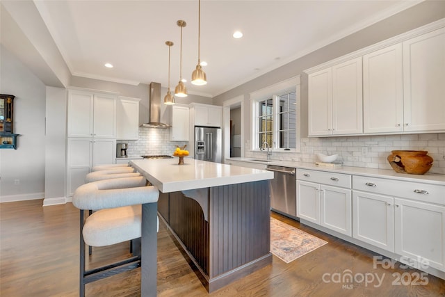 kitchen featuring a kitchen island, appliances with stainless steel finishes, white cabinets, wall chimney exhaust hood, and a sink