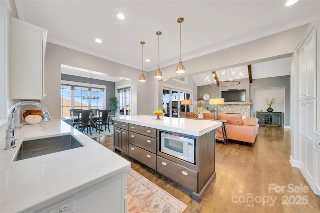 kitchen with light wood-type flooring, a sink, light countertops, built in microwave, and a chandelier