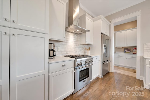 kitchen with high end appliances, light wood finished floors, light countertops, white cabinetry, and wall chimney exhaust hood