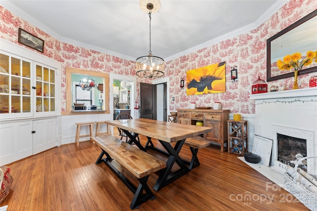 dining space with a brick fireplace, hardwood / wood-style floors, crown molding, and a chandelier