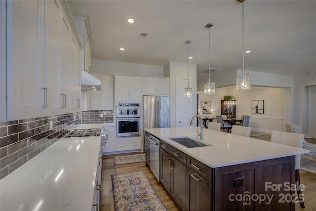 kitchen featuring pendant lighting, white cabinetry, sink, a kitchen island with sink, and stainless steel appliances