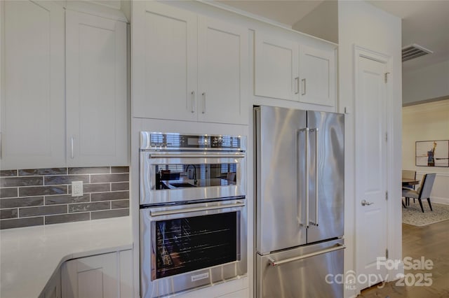 kitchen with white cabinetry, hardwood / wood-style flooring, tasteful backsplash, and appliances with stainless steel finishes