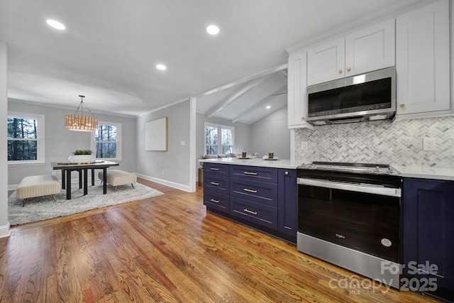 kitchen with blue cabinetry, lofted ceiling, white cabinets, stainless steel appliances, and backsplash