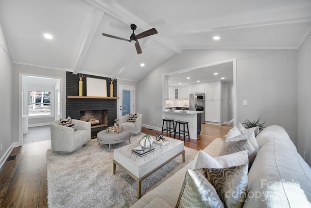 living room with lofted ceiling with beams, wood-type flooring, ceiling fan, and a fireplace