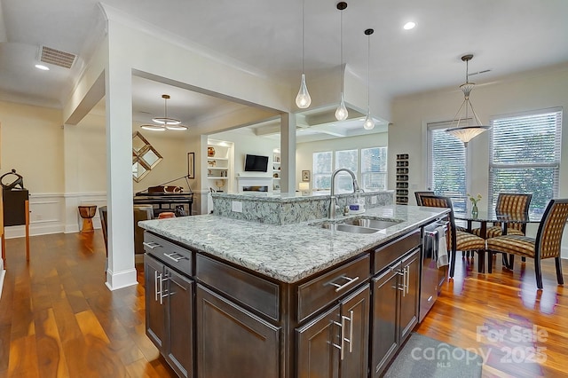 kitchen featuring pendant lighting, sink, a center island with sink, and light stone counters