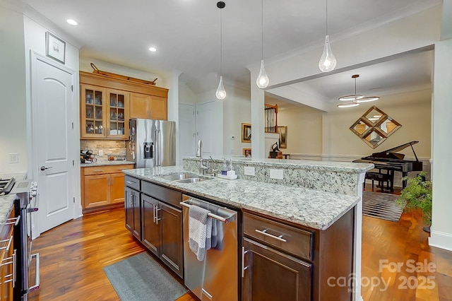 kitchen with pendant lighting, wood-type flooring, sink, a kitchen island with sink, and stainless steel appliances