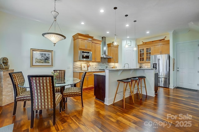 kitchen featuring backsplash, stainless steel fridge, a center island with sink, and wall chimney range hood