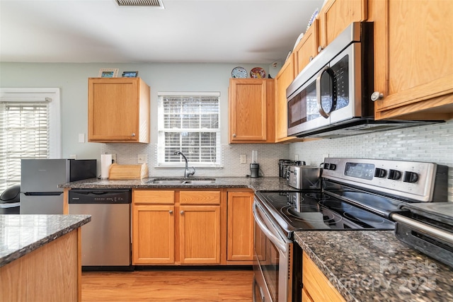 kitchen featuring a wealth of natural light, sink, dark stone counters, and appliances with stainless steel finishes