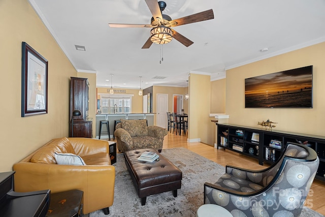 living room with light wood-type flooring, ceiling fan, and ornamental molding