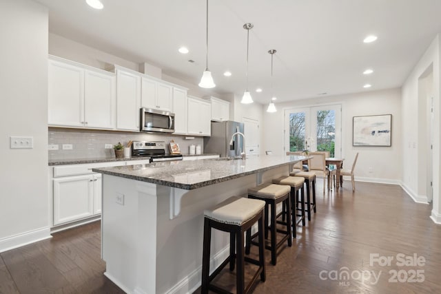 kitchen with decorative light fixtures, stainless steel appliances, an island with sink, and white cabinets