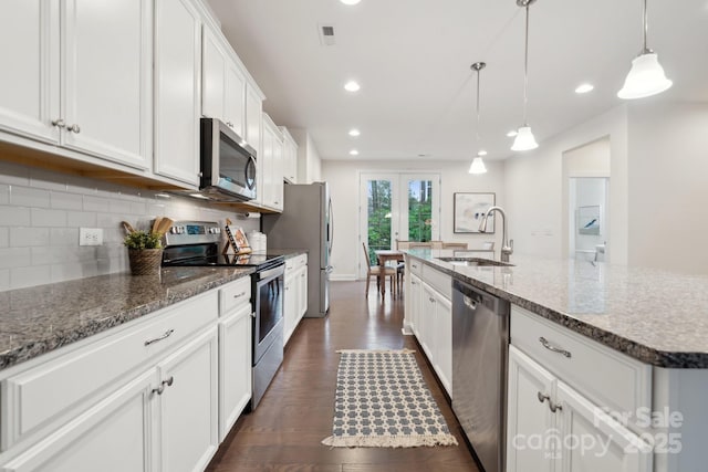 kitchen with sink, white cabinetry, hanging light fixtures, stainless steel appliances, and a center island with sink