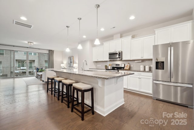 kitchen featuring white cabinetry, a center island with sink, light stone countertops, and appliances with stainless steel finishes