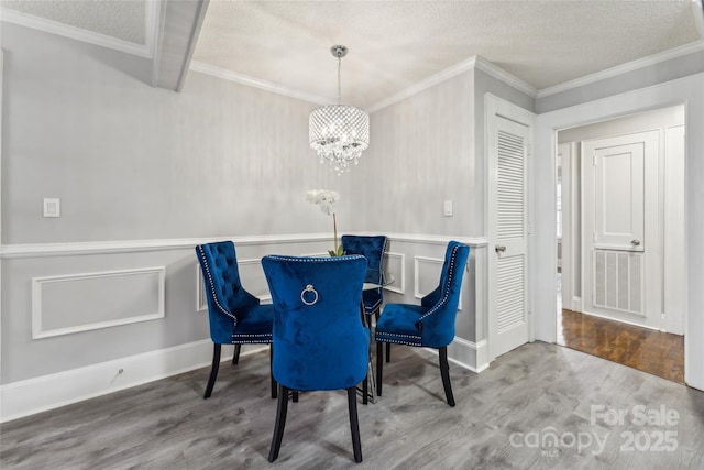 dining room with a textured ceiling, a notable chandelier, wood-type flooring, and crown molding