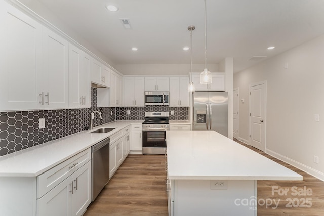 kitchen with sink, hanging light fixtures, stainless steel appliances, a center island, and white cabinets