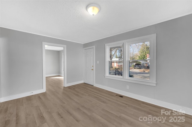 unfurnished room featuring light wood-type flooring, crown molding, and a textured ceiling