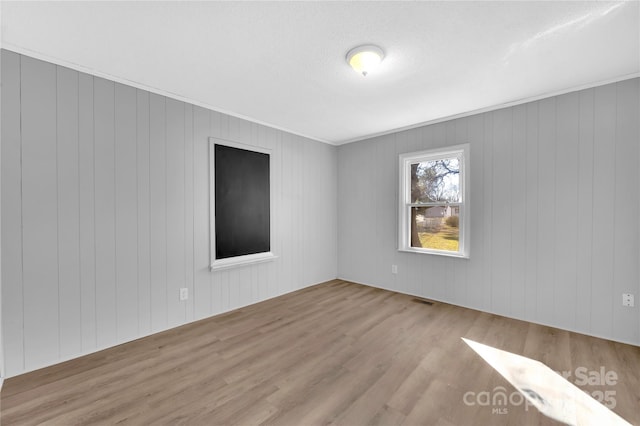 spare room featuring light hardwood / wood-style flooring and wood walls