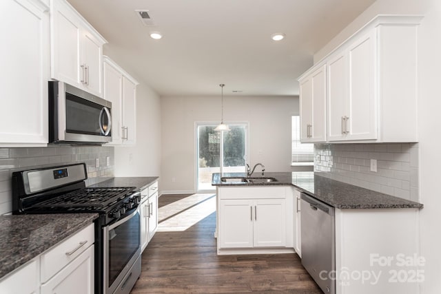 kitchen featuring kitchen peninsula, sink, appliances with stainless steel finishes, decorative light fixtures, and white cabinetry