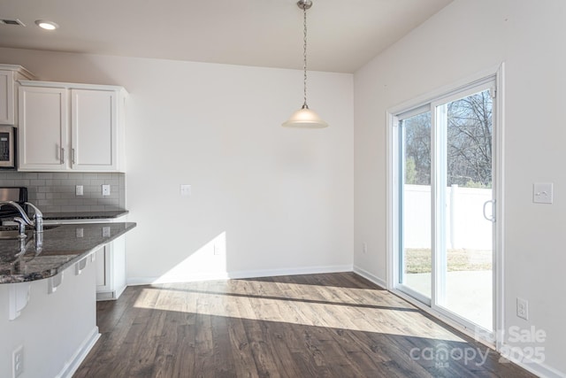 kitchen featuring white cabinetry, hanging light fixtures, backsplash, dark stone counters, and wood-type flooring