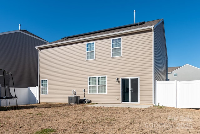 rear view of property featuring central air condition unit, a lawn, a patio, and a trampoline