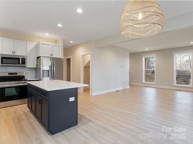 kitchen with stainless steel appliances, a kitchen island, an inviting chandelier, light hardwood / wood-style floors, and white cabinetry