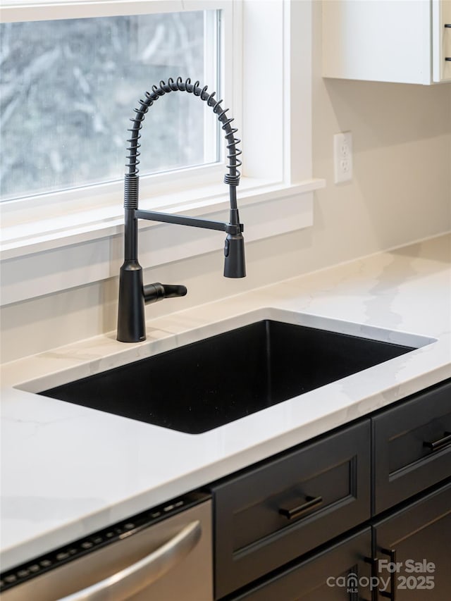 room details with light stone countertops, white cabinetry, stainless steel dishwasher, and sink