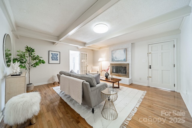 living room with a brick fireplace, a textured ceiling, light hardwood / wood-style flooring, and beamed ceiling