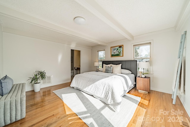 bedroom with light wood-type flooring, a textured ceiling, and beamed ceiling