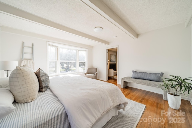 bedroom featuring wood-type flooring, beam ceiling, and a textured ceiling