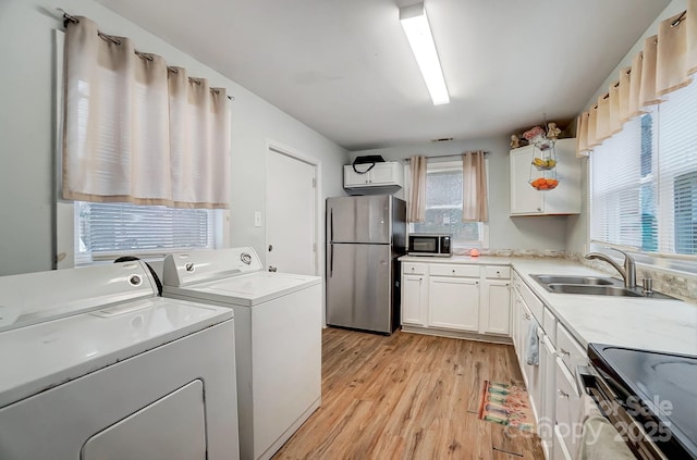 laundry area with light wood-type flooring, washer and clothes dryer, and sink