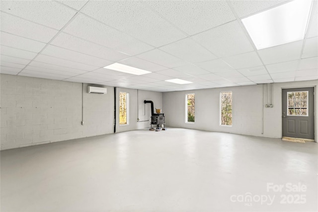 basement with a drop ceiling, a wood stove, and a wall unit AC