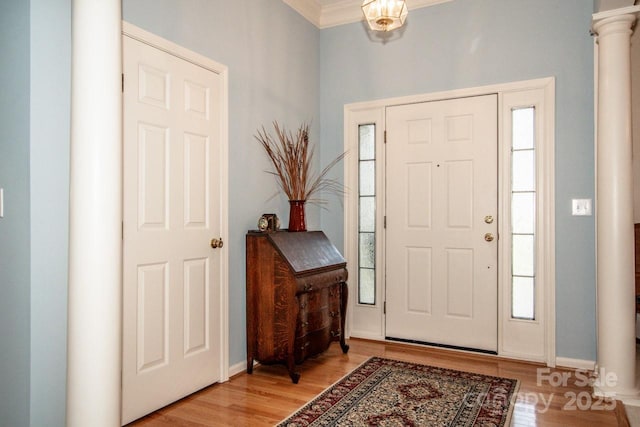 entrance foyer with ornate columns, ornamental molding, and light wood-type flooring