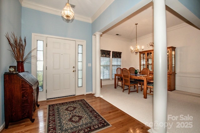 foyer with a notable chandelier, ornamental molding, wood-type flooring, and ornate columns