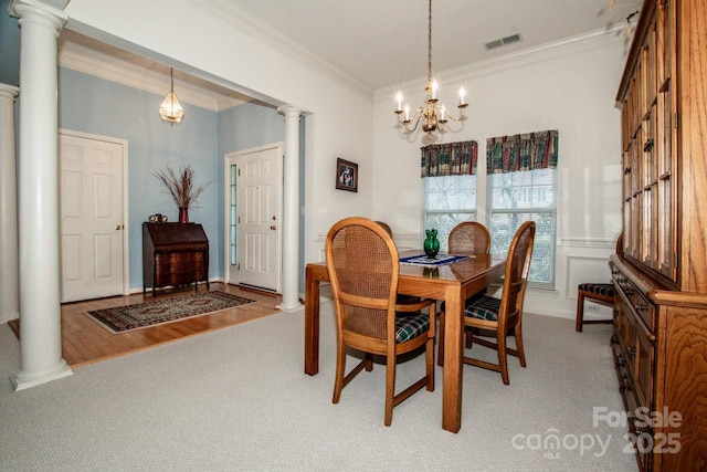 carpeted dining area with decorative columns, crown molding, and a chandelier