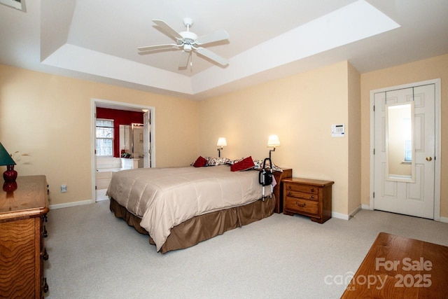 carpeted bedroom featuring ceiling fan, ensuite bath, and a tray ceiling