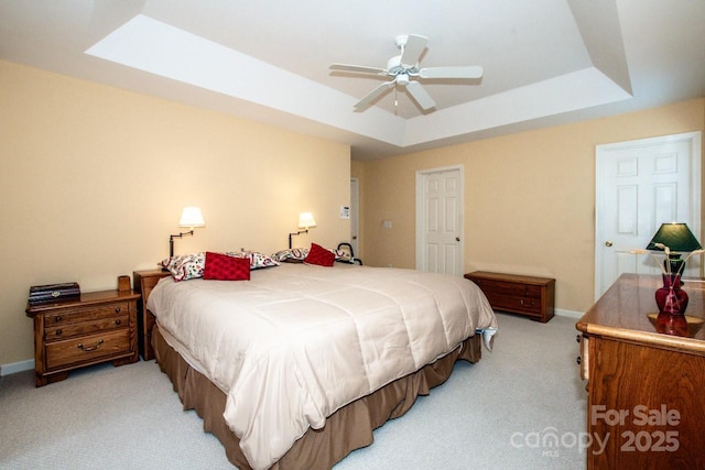 bedroom featuring a skylight, light colored carpet, a raised ceiling, and ceiling fan