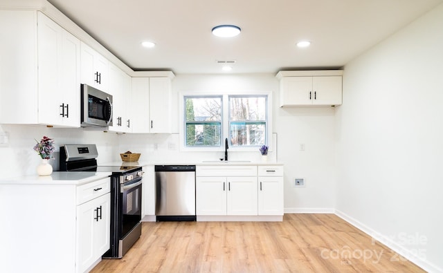 kitchen featuring appliances with stainless steel finishes, tasteful backsplash, white cabinetry, sink, and light hardwood / wood-style floors