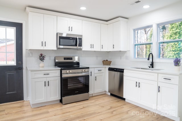 kitchen featuring sink, light hardwood / wood-style flooring, white cabinetry, stainless steel appliances, and tasteful backsplash