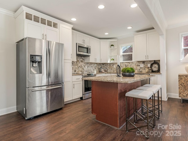 kitchen featuring a kitchen island, a kitchen bar, white cabinetry, appliances with stainless steel finishes, and light stone counters