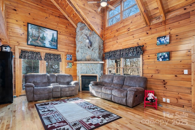 living room featuring wooden walls, beamed ceiling, a ceiling fan, and hardwood / wood-style flooring