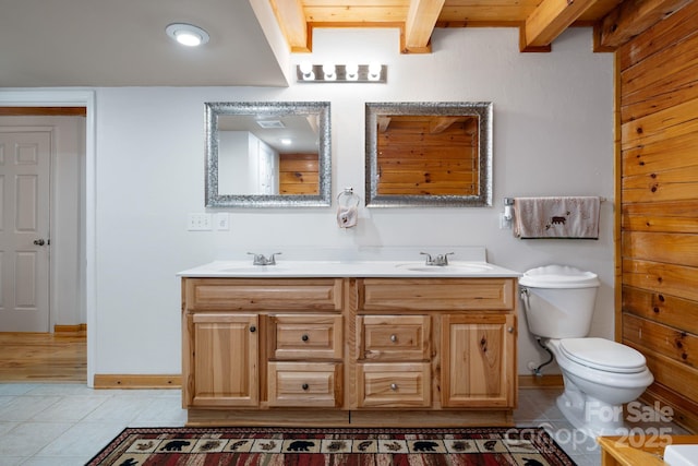 full bath featuring tile patterned flooring, beamed ceiling, toilet, double vanity, and a sink