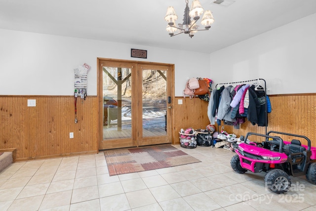 entryway with a notable chandelier, a wainscoted wall, tile patterned flooring, and wooden walls